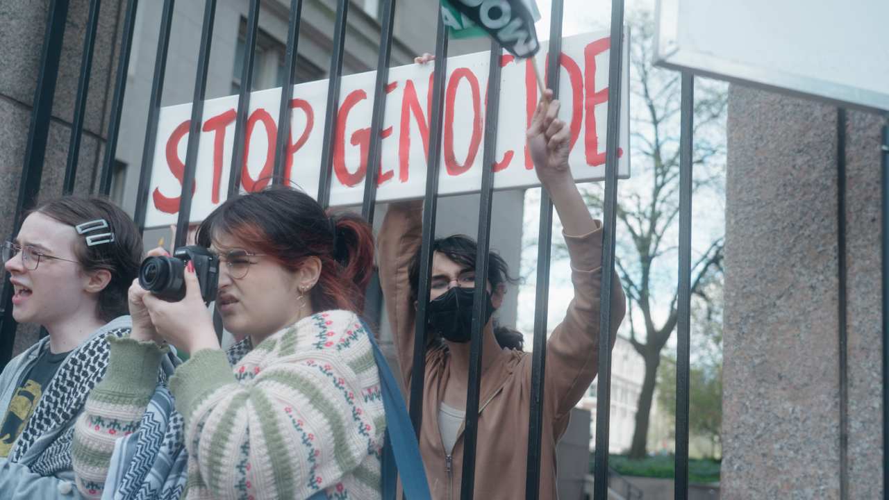 a person holding a protest sign from behind a gate